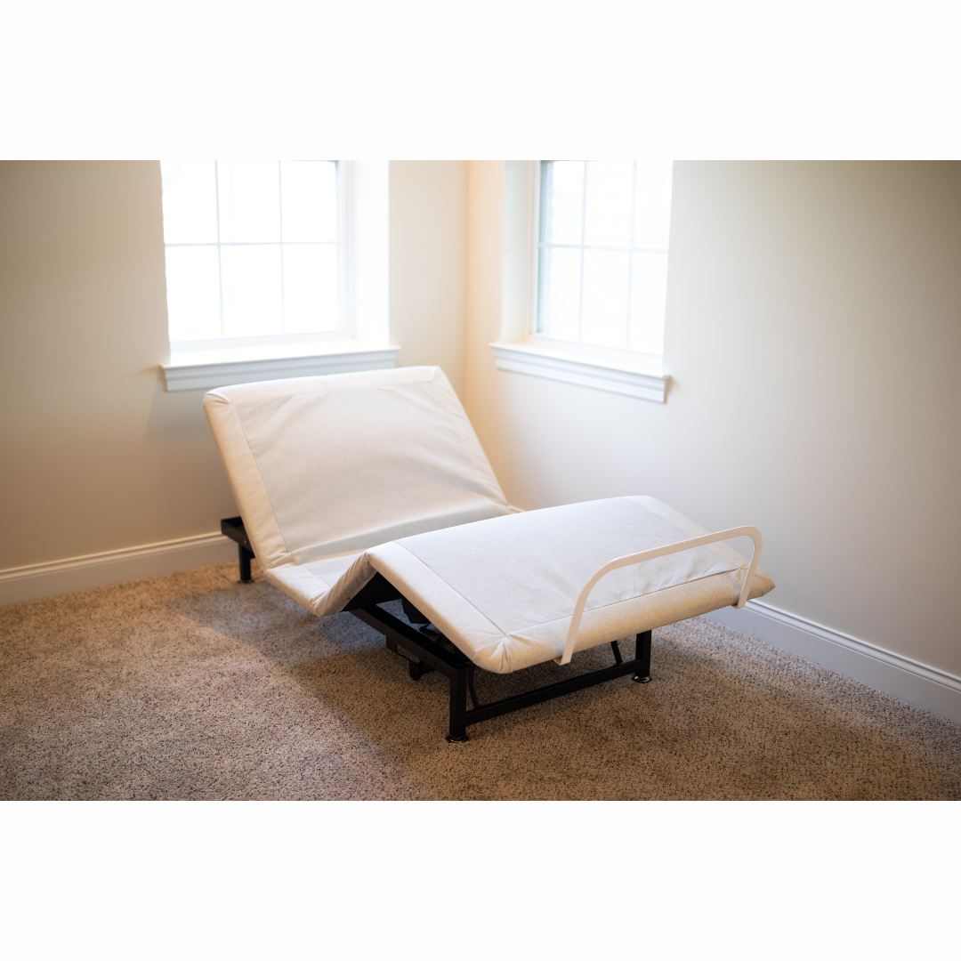 The Flexabed Value-Flex Adjustable Bed, featuring a premier mattress, is arranged in a carpeted room. Its black frame offers adjustable heights, and the head and foot sections are elevated. Light from two white-framed windows enhances the versatility of this sleep solution.